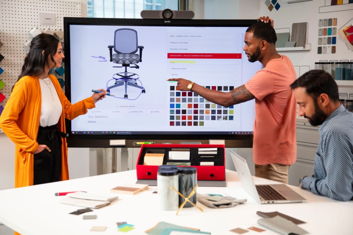 Creative workplace meeting with a SMART board displaying chair design options. Team members are selecting materials and colors, focusing on design details for a customizable office chair.