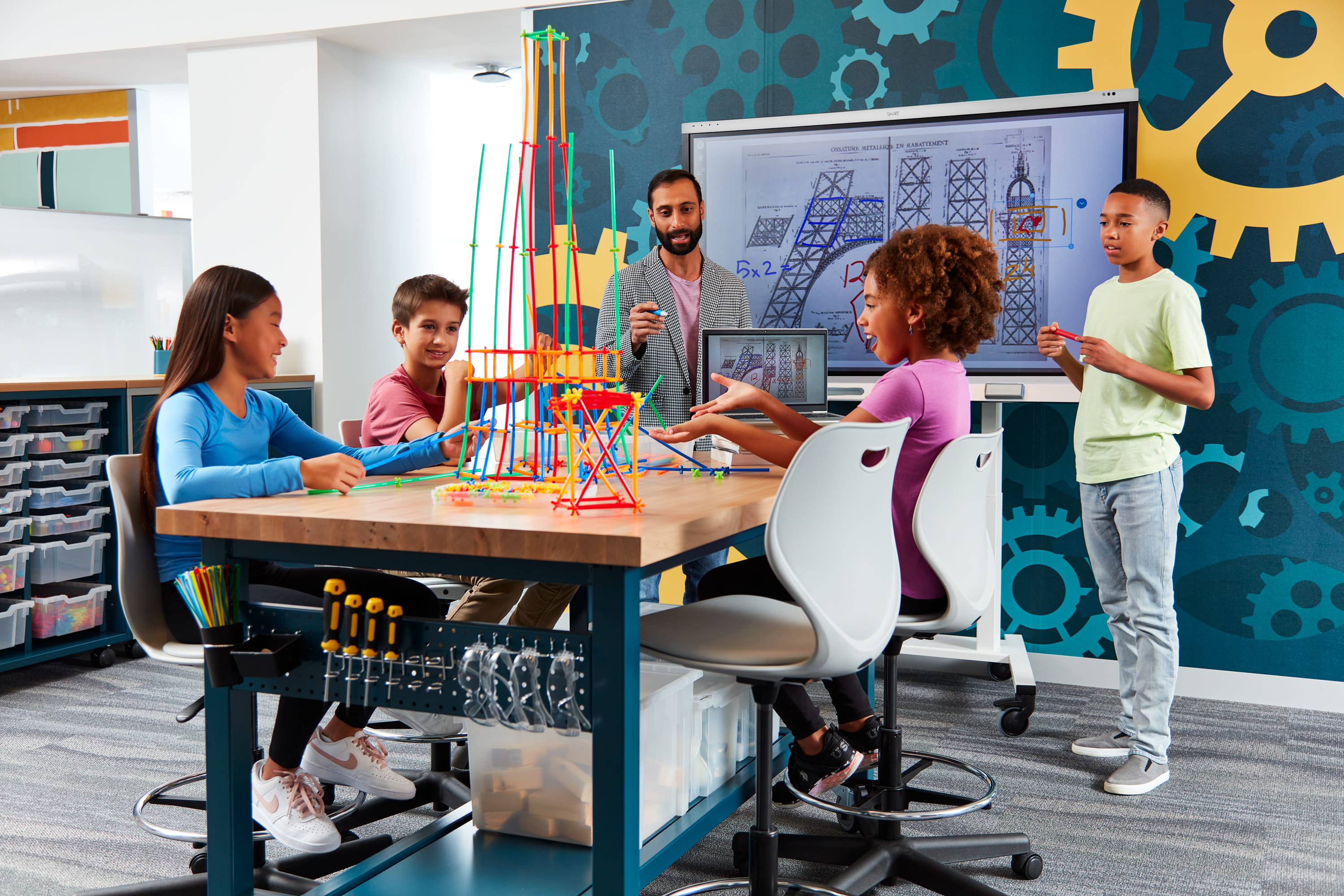 Students engaging in a creative STEM project with a SMART board in the background, showcasing interactive learning.