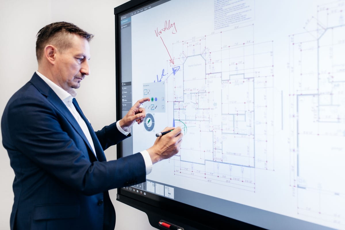 Businessman using SMART Ink to interact with a SMART Board during a presentation, showcasing detailed architectural plans.