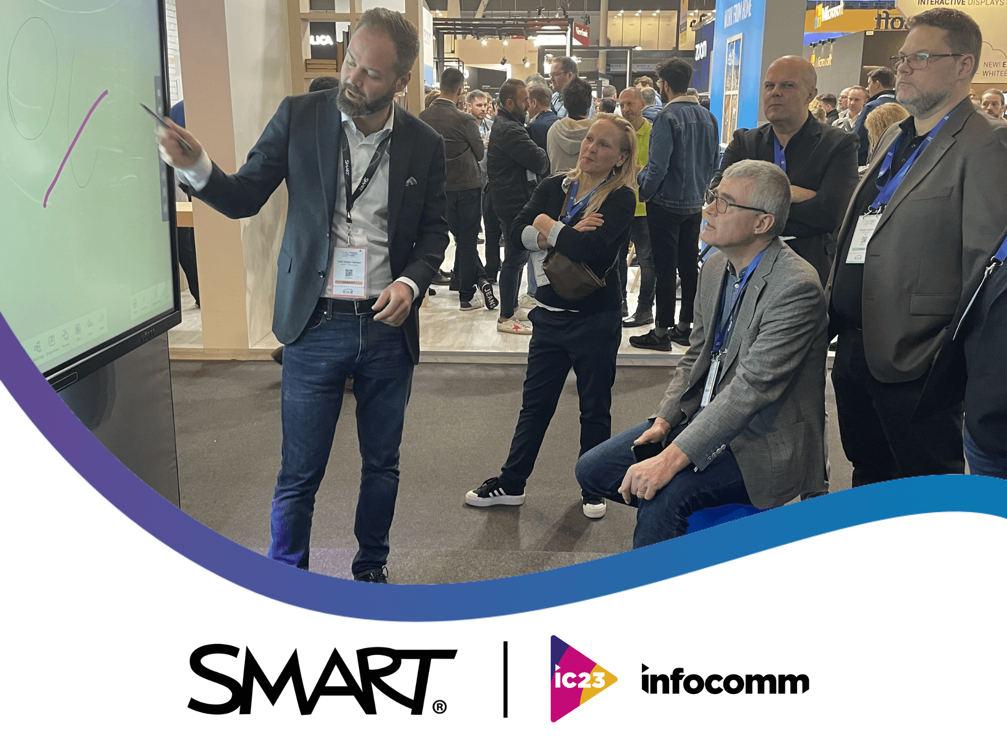 SMART team demonstrating the SMART interactive display to a business professional at InfoComm 2023, with SMART and Infocomm logos displayed at the bottom of the image.