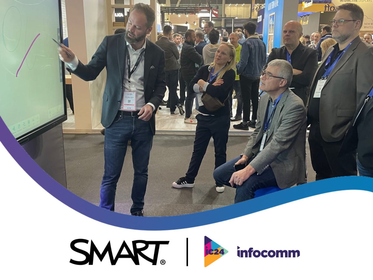 SMART team demonstrating the SMART interactive display to a business professional at InfoComm, with SMART and Infocomm logos displayed at the bottom of the image.