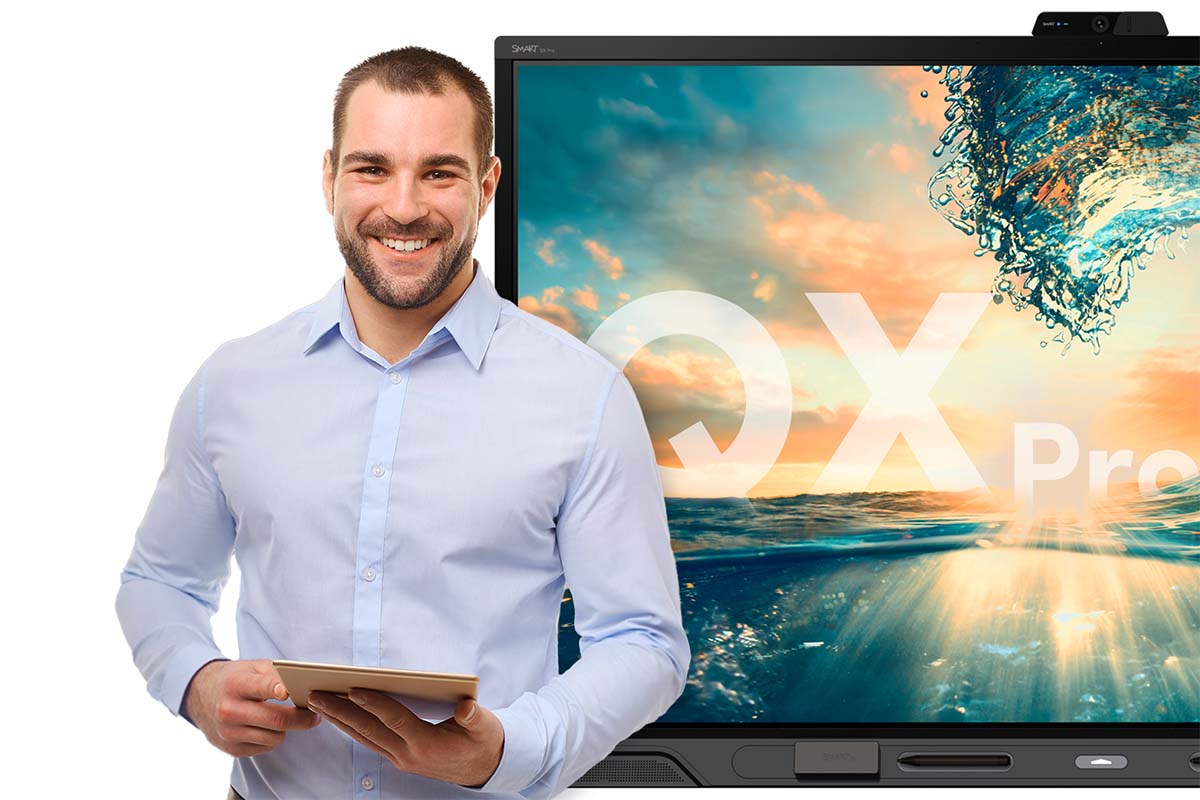 Smiling man in a light blue shirt holding a tablet in front of a SMART Board® QX Pro series interactive display, which is presenting a vivid and colorful aquatic-themed image.