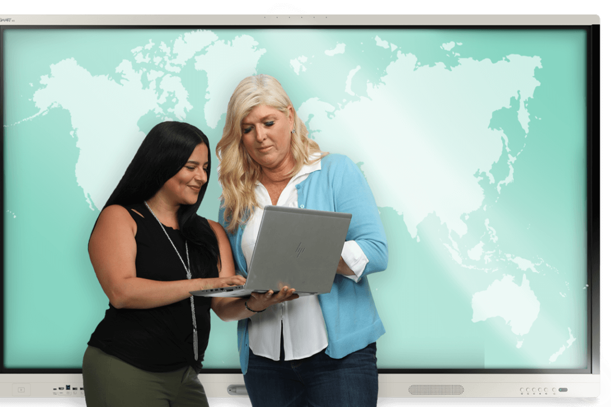 Two colleagues, one holding a laptop, are discussing strategies in front of a SMART board with a world map, symbolizing global connectivity and the integration of technology in modern business practices.