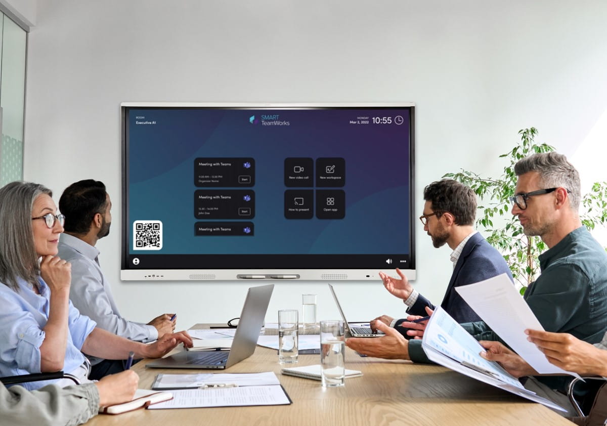 Professionals in a meeting room engaging with the SMART TeamWorks™ display, showcasing easy one-touch access to Microsoft Teams meetings and cloud storage.