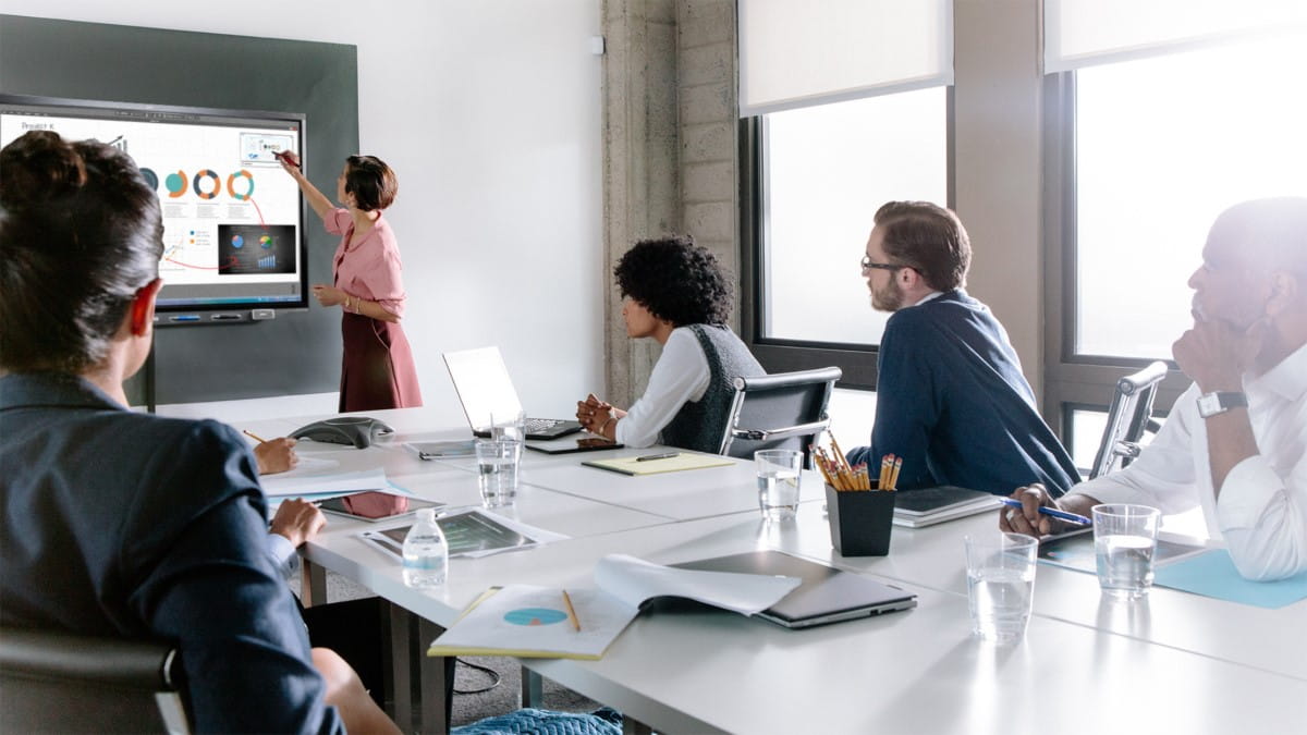 A group of five professionals working collaboratively in a meeting room, using annotations to markup their documents on a SMART Interactive Display.