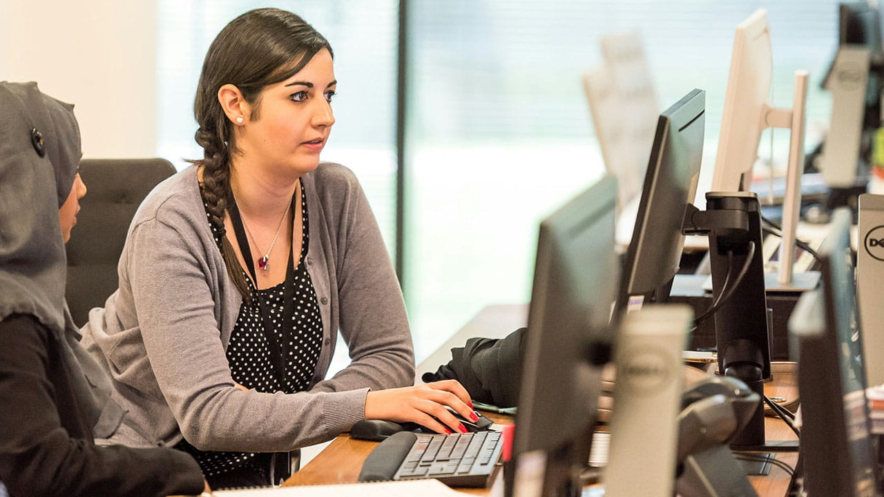 Two women collaborating in a modern office using desktop computers.