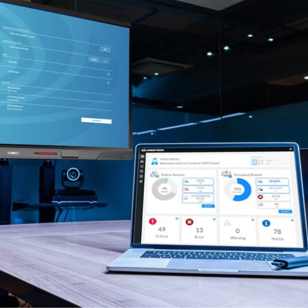 Laptop on a conference room table displaying a management dashboard with metrics, with a video conferencing camera and a SMART board in the background.