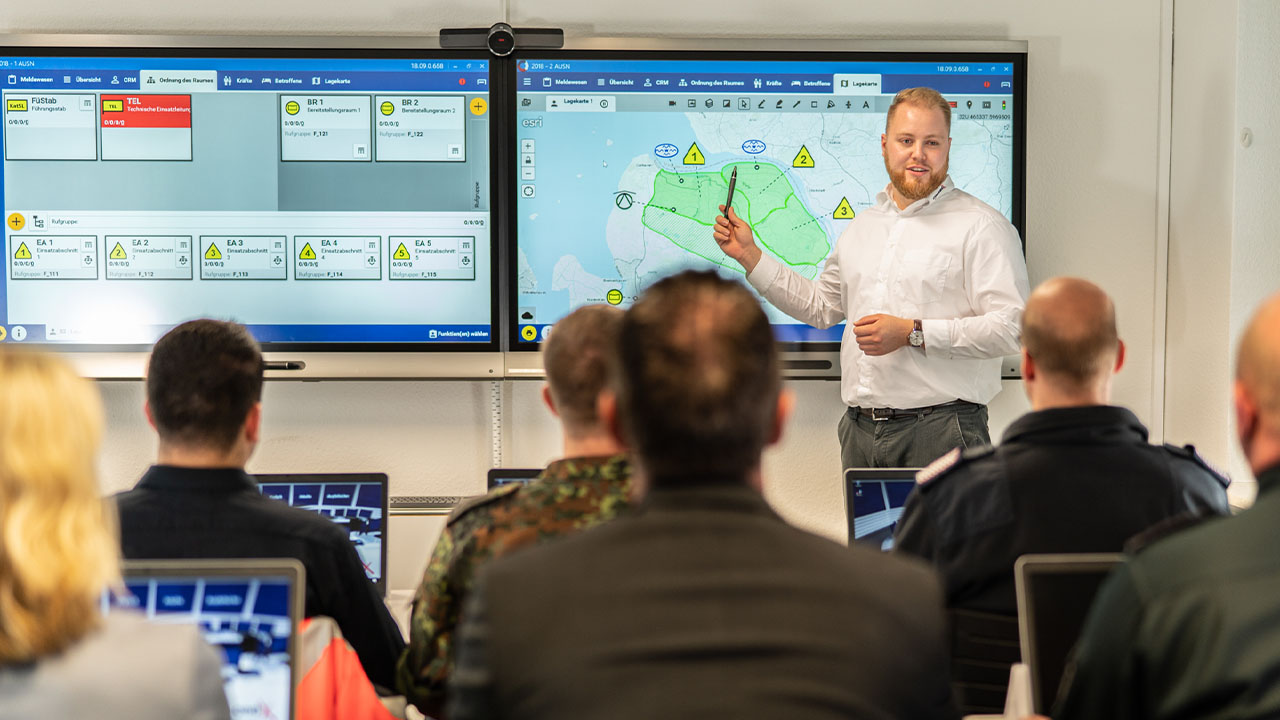 Instructor leading a training session on public safety using SMART interactive displays, with participants viewing displayed maps and data.