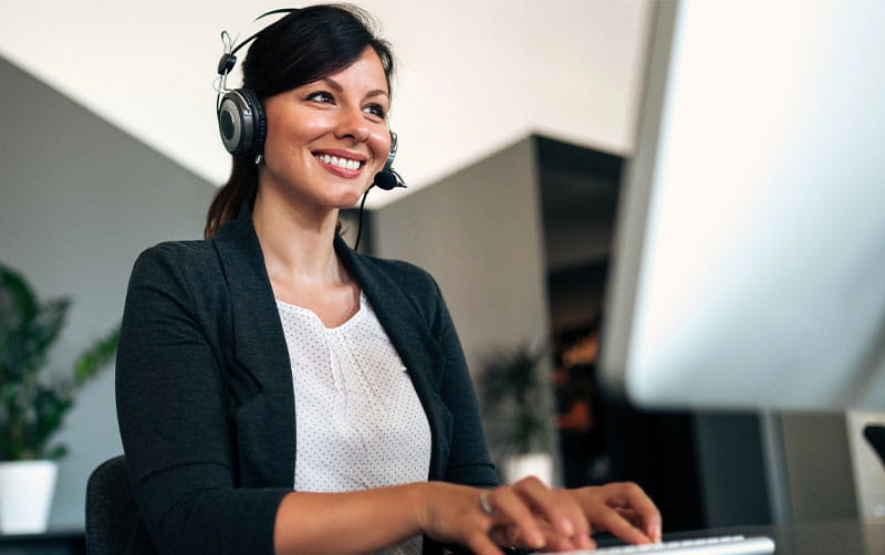 A happy tech support woman with headphones on, engaged in assisting customers.