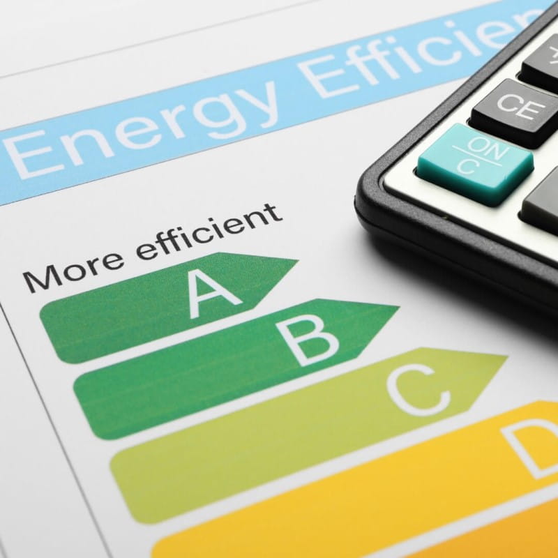 Close-up of an energy efficiency rating chart ranging from green 'A' for 'More efficient' to yellow and red grades, next to a calculator.