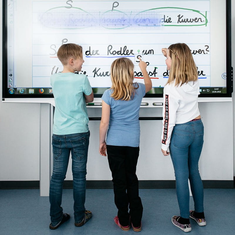 Three children actively engaged in a classroom activity, collaboratively utilizing a SMART board as a tool for interactive learning and participation.