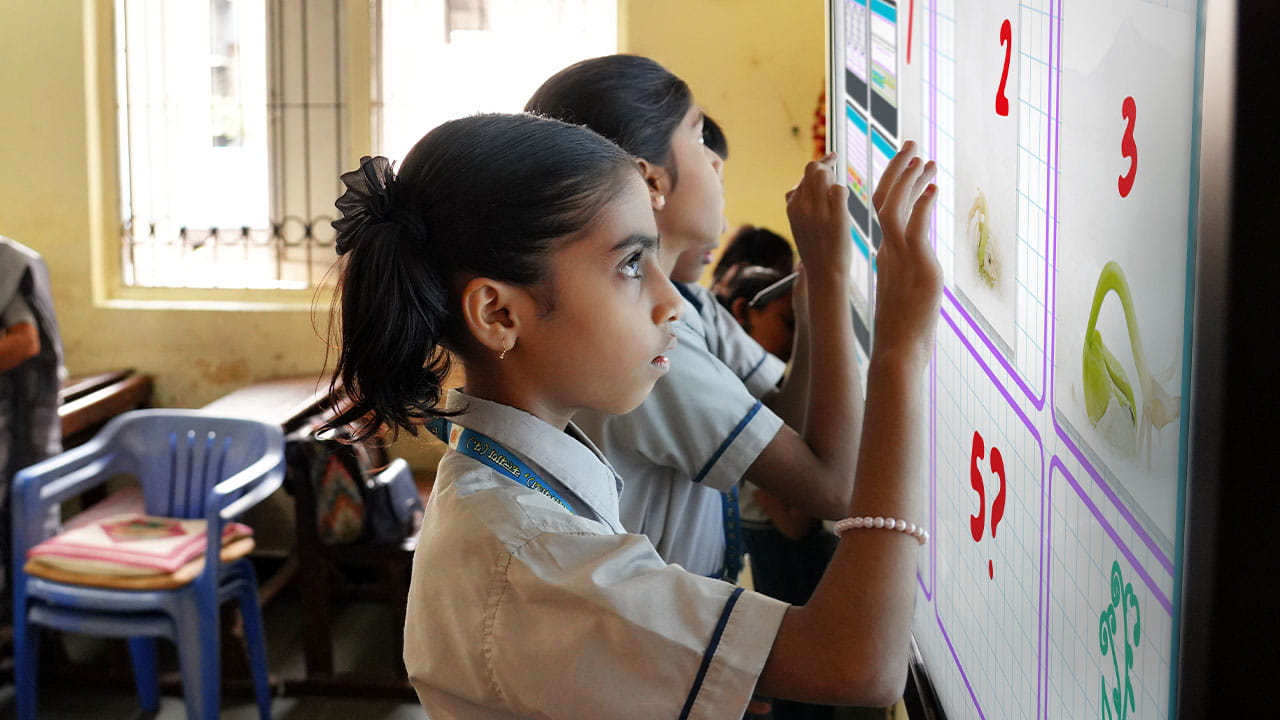 A young student in uniform interacting with a SMART Board, attentively engaging in an activity in a classroom.