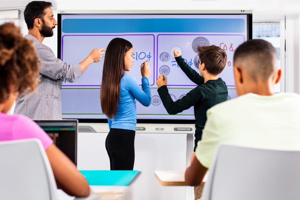 Teacher and students interactively learning with a SMART board, demonstrating hands-on educational technology.