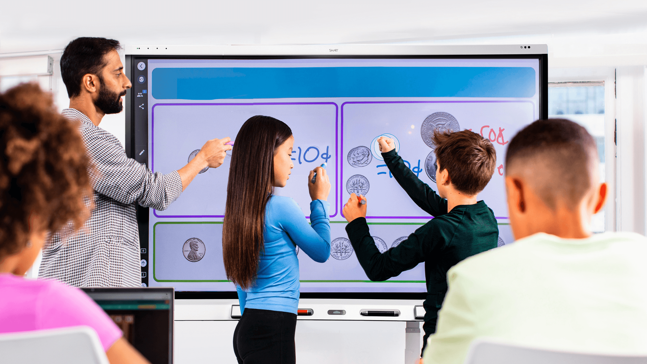 An interactive display being used by a teacher and two students for collaborative learning.