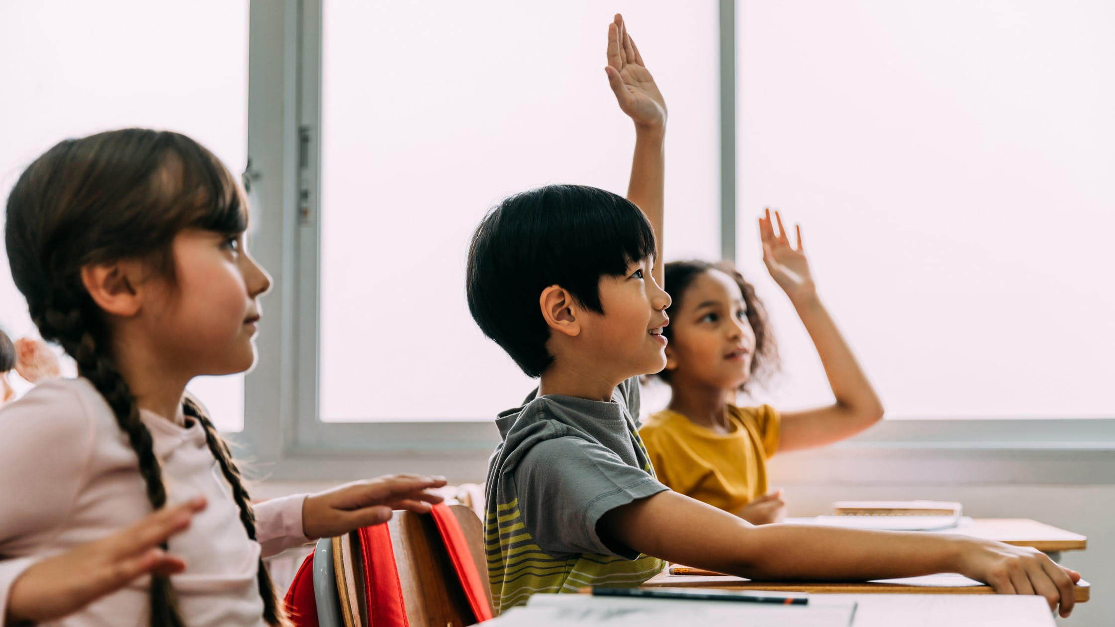Children actively engaged in a classroom setting, raising their hands and participating in learning activities.