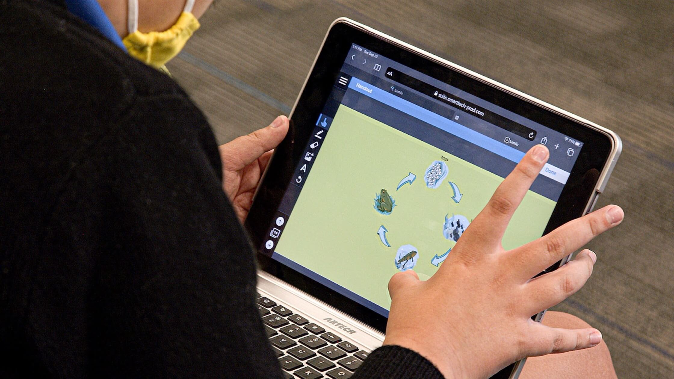 A touch screen laptop showing a Lumio lesson on the screen, while the hands of a student interacts with the content in the lesson.