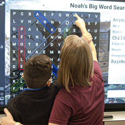 A teacher and student performing a crossword puzzel on a SMART board.
