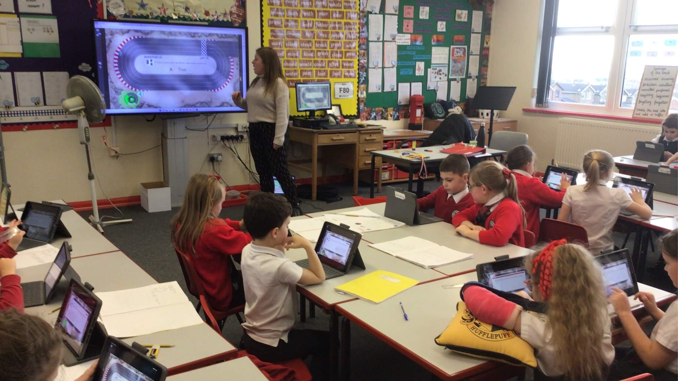 Alt text:	A classroom at Sandford Hill Primary School showcasing students working on their student devices and a teacher instructing on her SMART Board.
