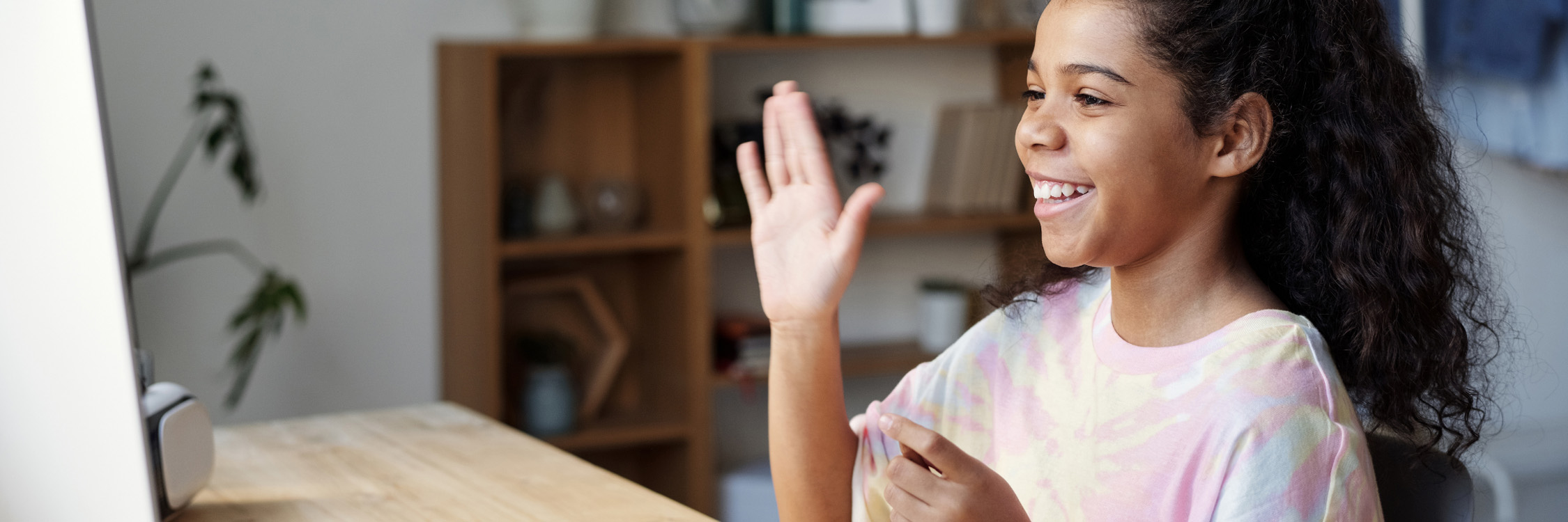 A young student waving hello while connecting to her class, remotely.