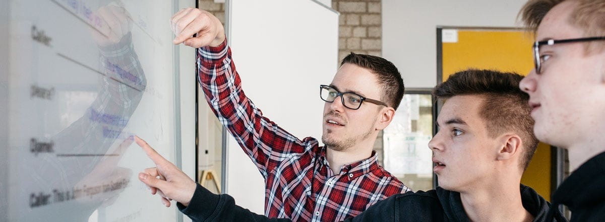 Engaged discussion between a teacher and students in front of a SMART Board.