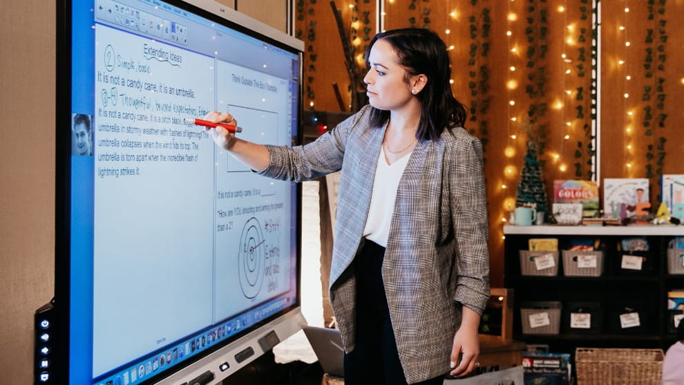 An educator stands in front of a SMART board, while engaging with students.