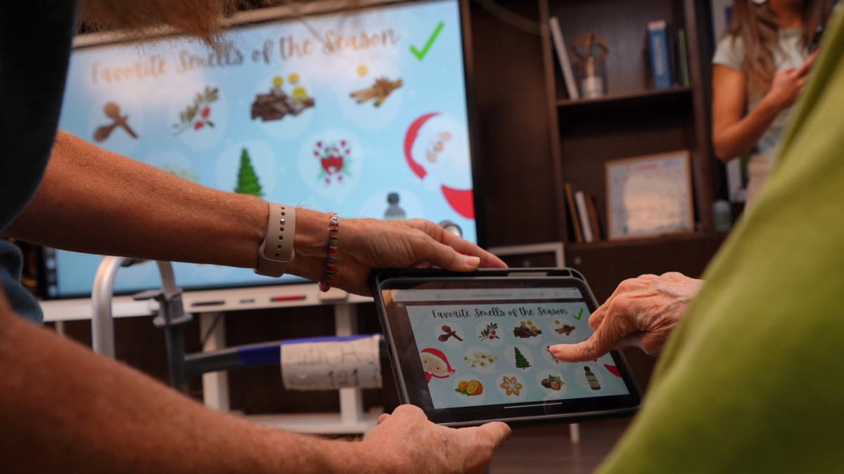 A senior care resident's hand, interacting with a tablet that is reflected on a SMART Display.