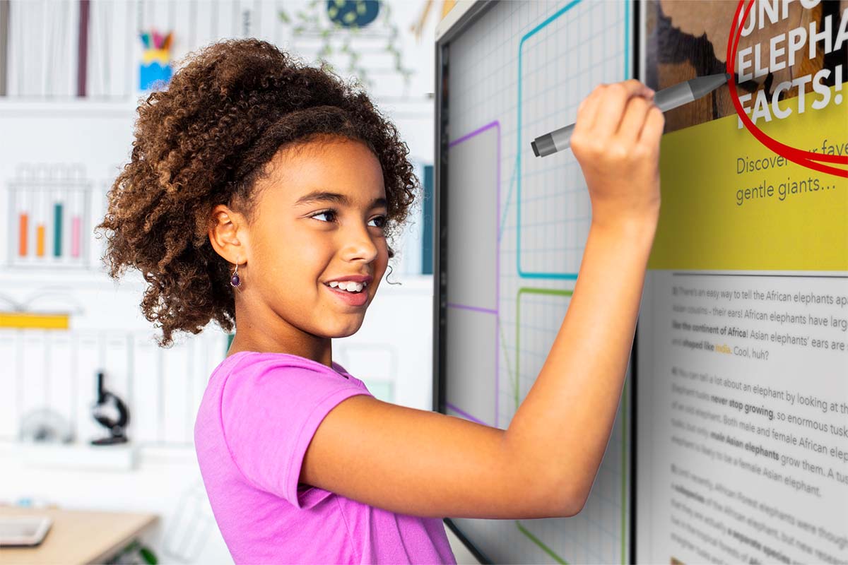 Smiling young student using SMART ink on a SMART Board displaying educational content in a bright classroom setting.