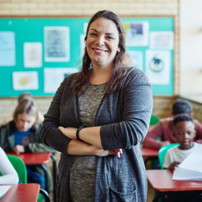 A teacher stands at the front of the classroom with her students working independently behind her.