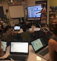 A teacher at the front of the room with a SMART board 