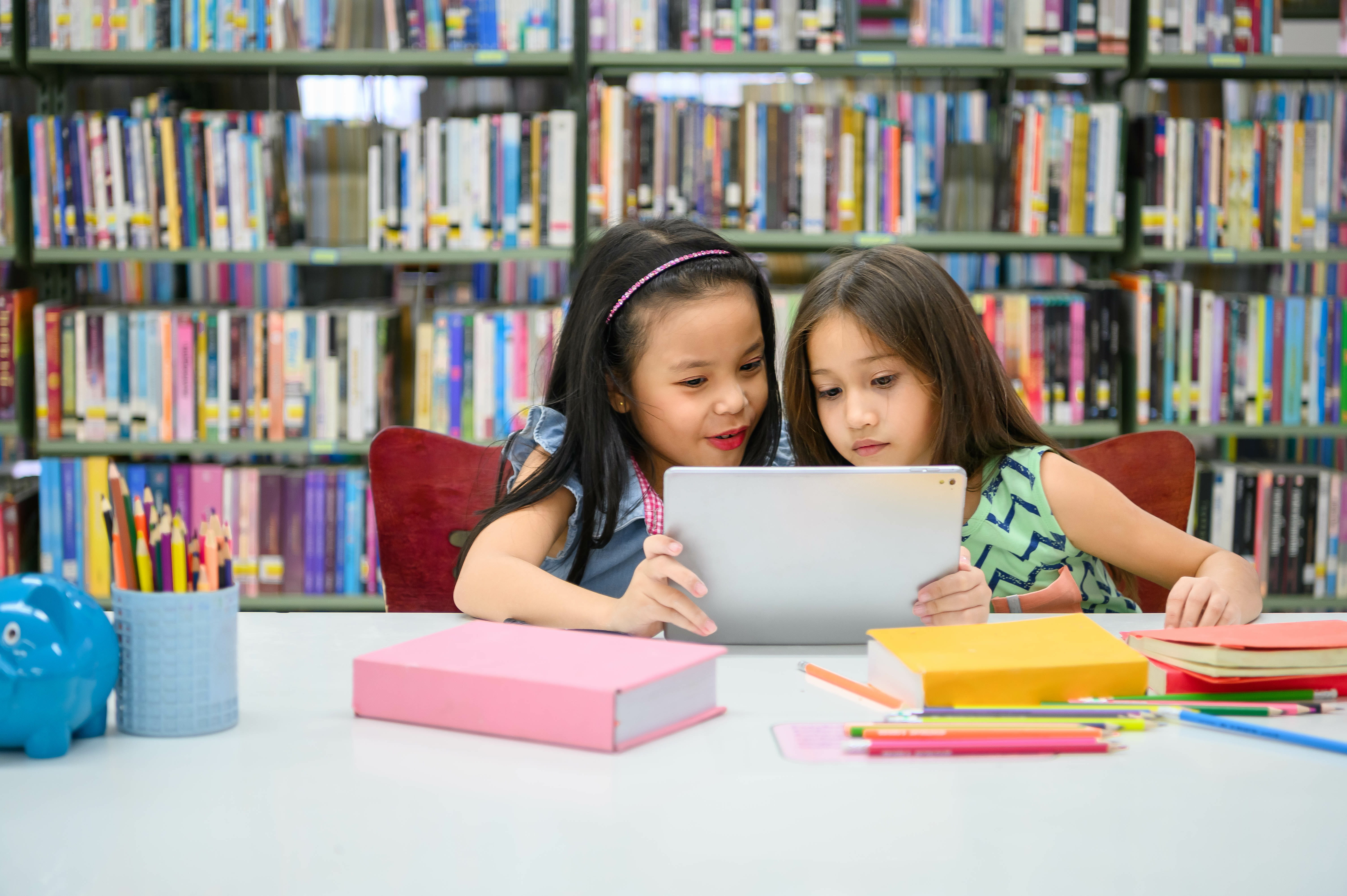Two elementary students collaborate on a digital assignment at their school's library.