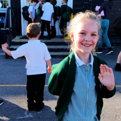 Student waving hello in front of a school building