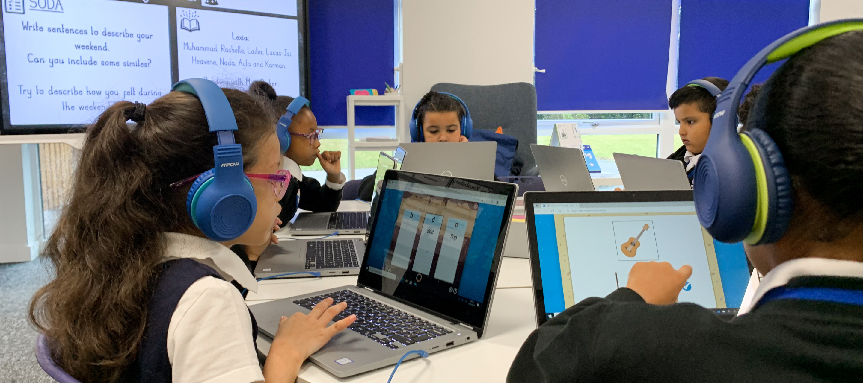 A group of students working on their students devices with a connected SMART Display in the background