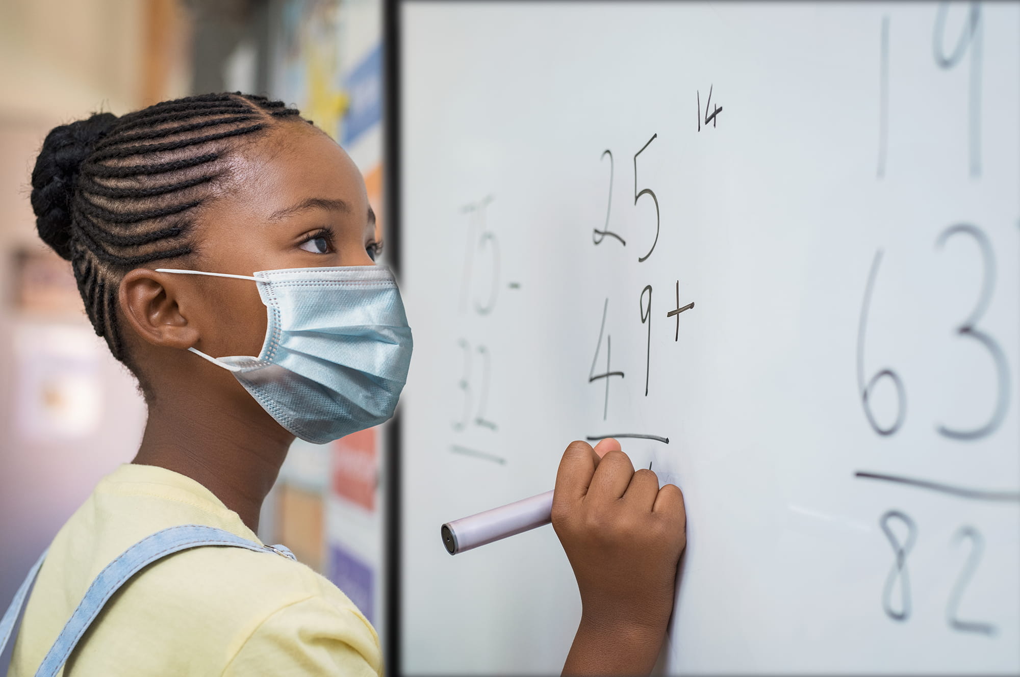 A student works on a math problem at a whiteboard while wearing a mask.