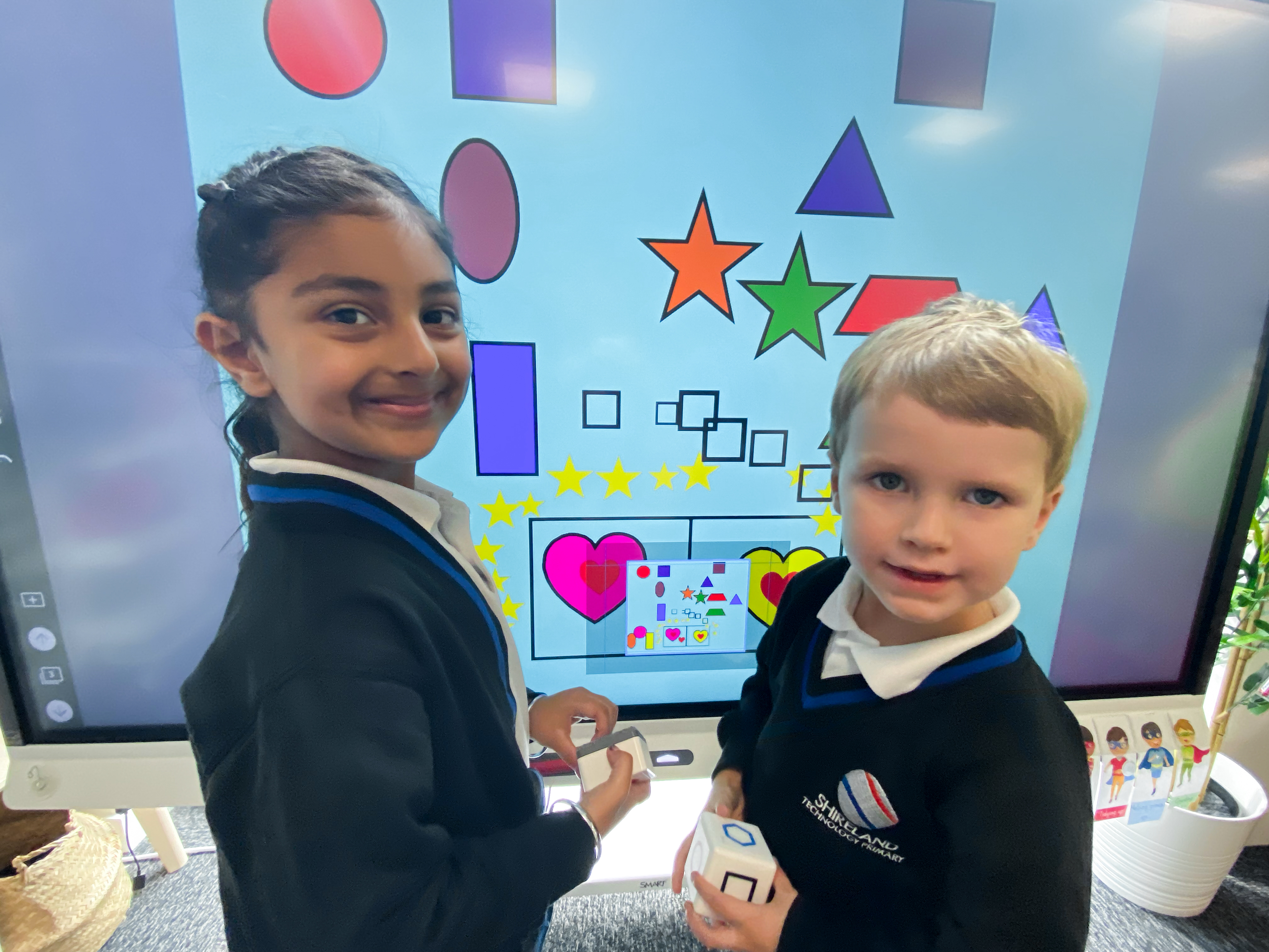 Two elementary students smile while completing a lesson with manipulatives at the SMART Board. 