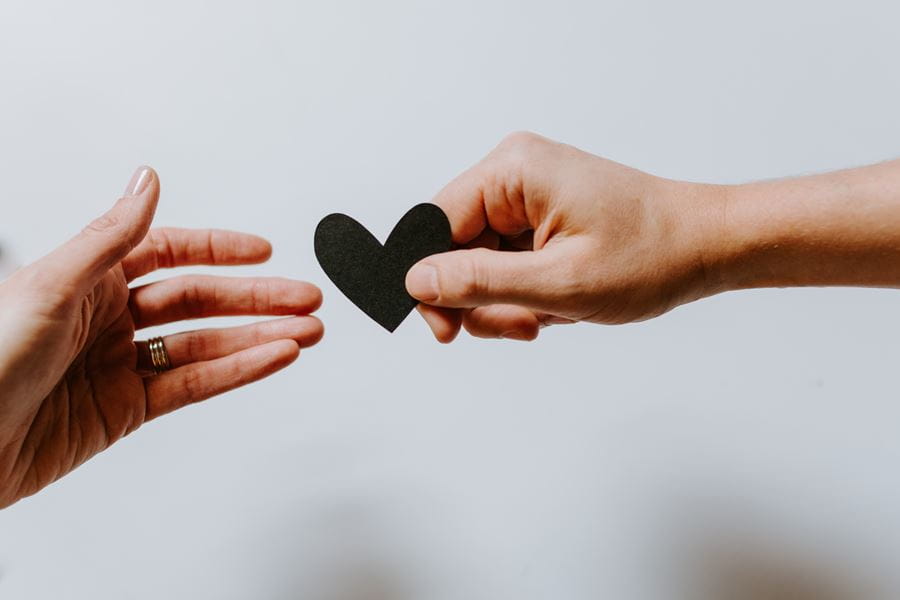 A hand sharing a cut-out of a black heart with another