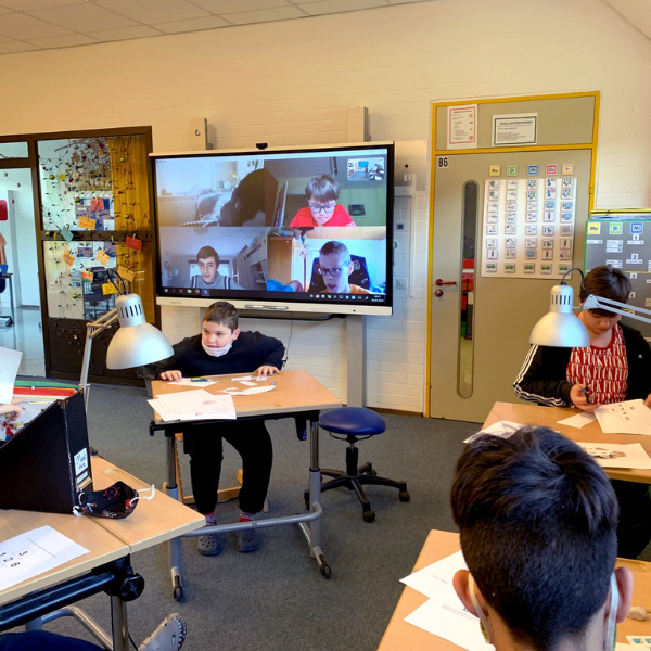 Students connecting in-person and virtually in a classroom using a SMART Board.