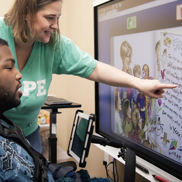 An educator assisting a special-needs student with interactive technology. 