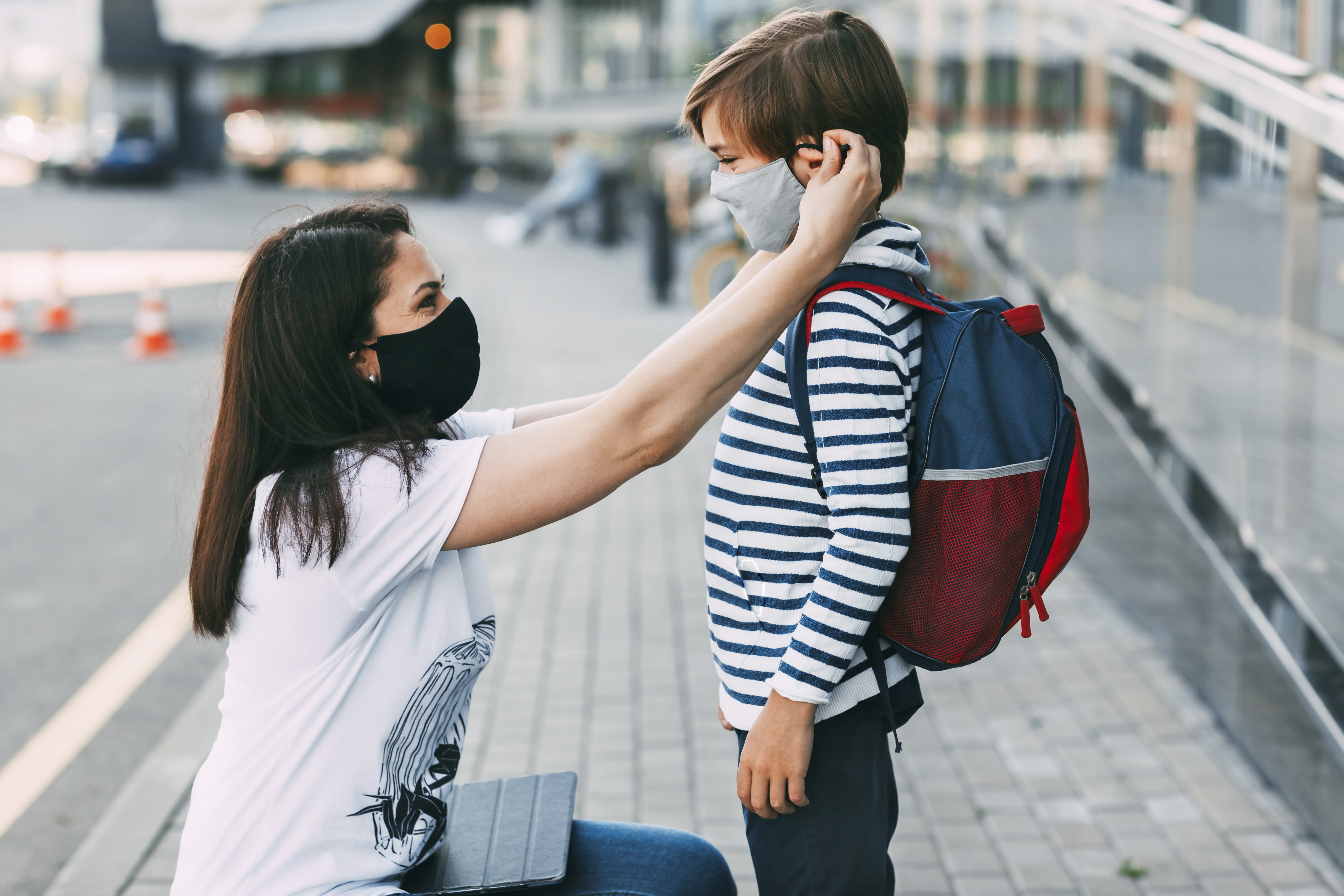 A teacher helps an elementary ages student replace his mask.