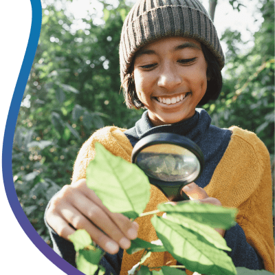Young boy examining a leaf with a magnifying glass outdoors.