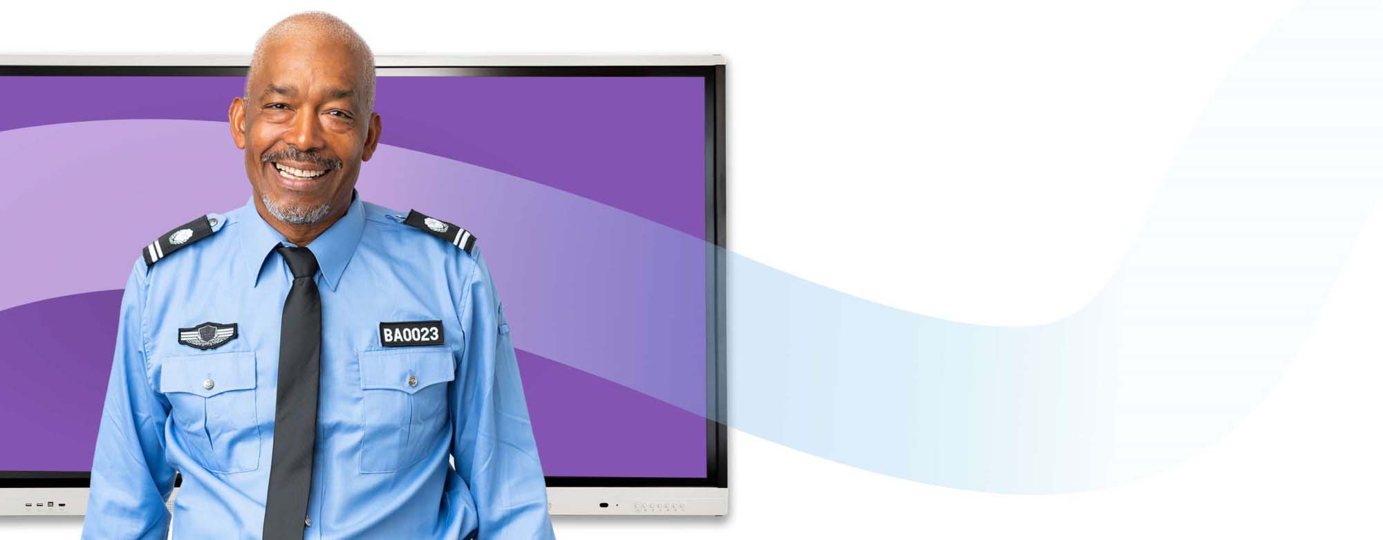 A security officer in blue uniform smiling confidently while standing next to a SMART Board interactive display, which is off to the side in the image.