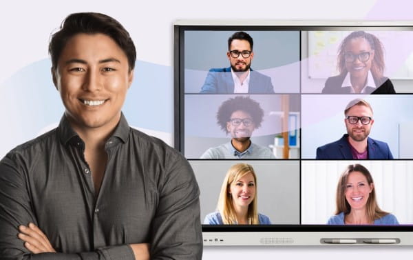 Professional smiling in front of an interactive display showing a virtual team meeting with six participants.