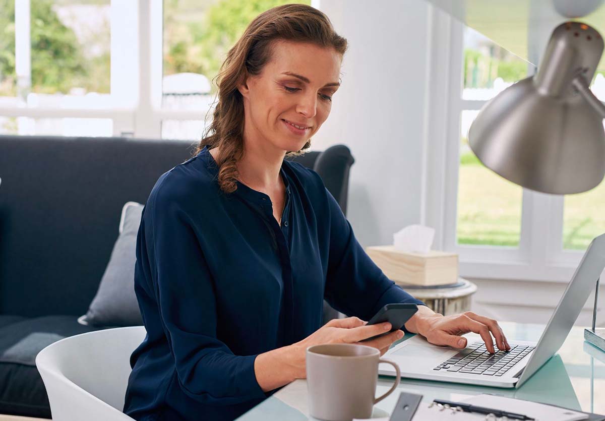 A professional woman using a laptop and smartphone to facilitate a digital meeting, embodying the seamless integration of technology for efficient brainstorming and collaboration.