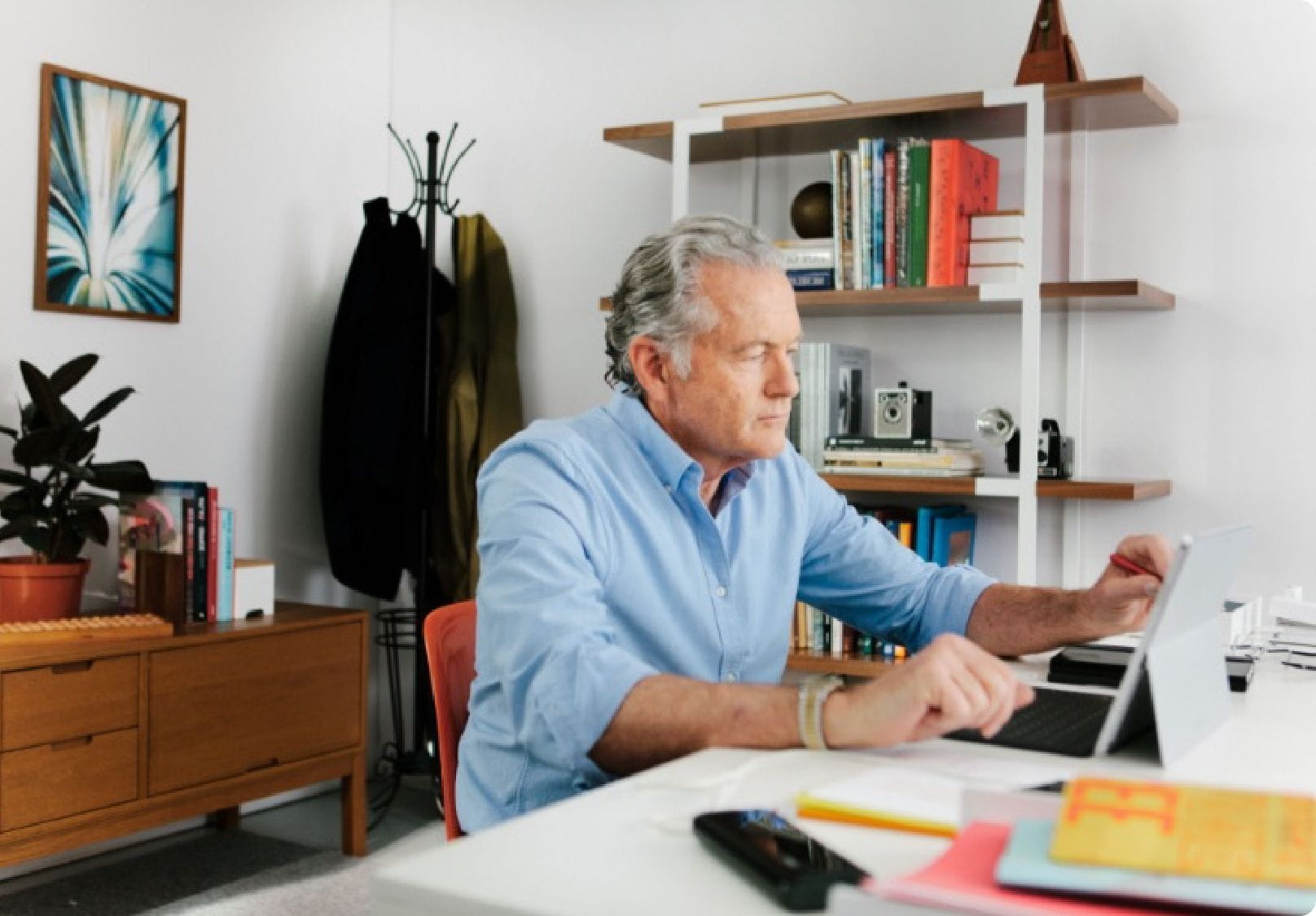 An older man working from home, focused on annotating a digital document on his tablet, exemplifying remote collaboration as part of a business strategy.