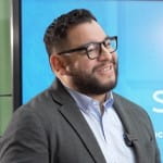 Mark Mendoza, wearing glasses and a suit in a candid interview moment. 