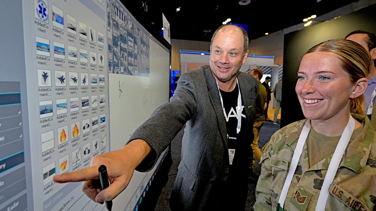 A SMART representative demonstrating an interactive SMART Board to a military personnel during a trade show.