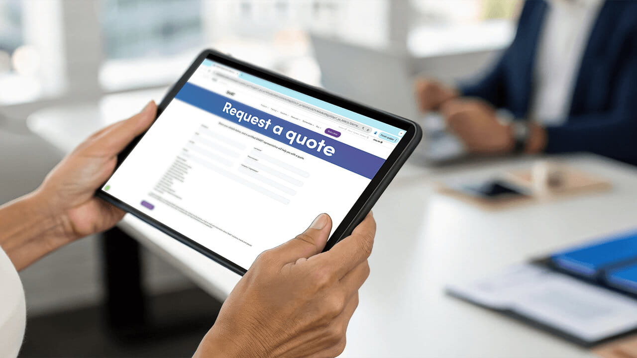 A person holding a tablet displaying the SMART 'Request a Quote' page, showcasing fields for submitting education/k-12 details
