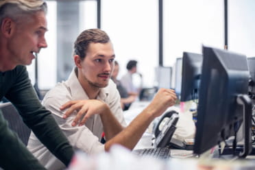 Two colleagues discussing a project with focus and collaboration at a computer workstation in a modern office environment.