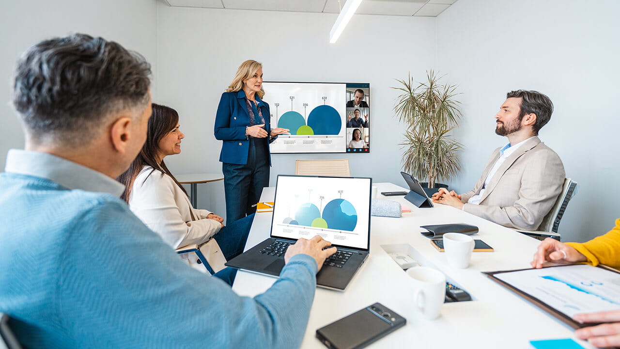DSN series display used during a hybrid business meeting, with in-room participants viewing presentation data and remote attendees joining by video conference.