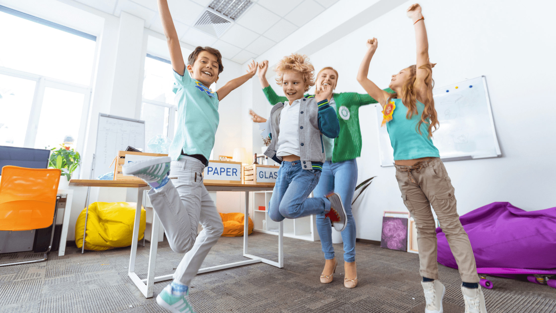 Three students and their teacher jumping in a classroom.