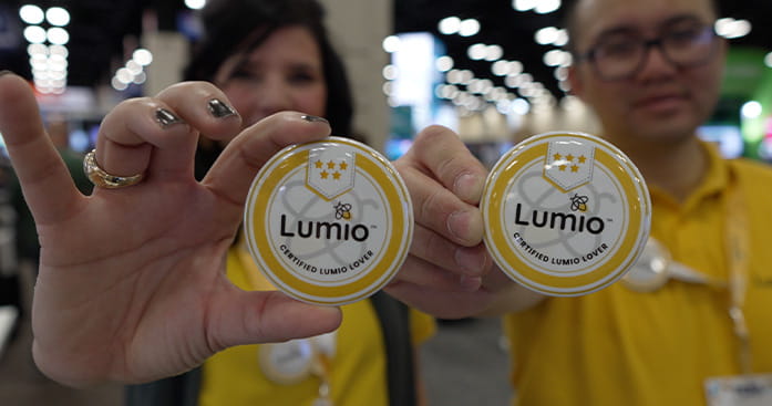 Two people holding up Lumio buttons that say 'Certified Lumio Lover' at an educational event.